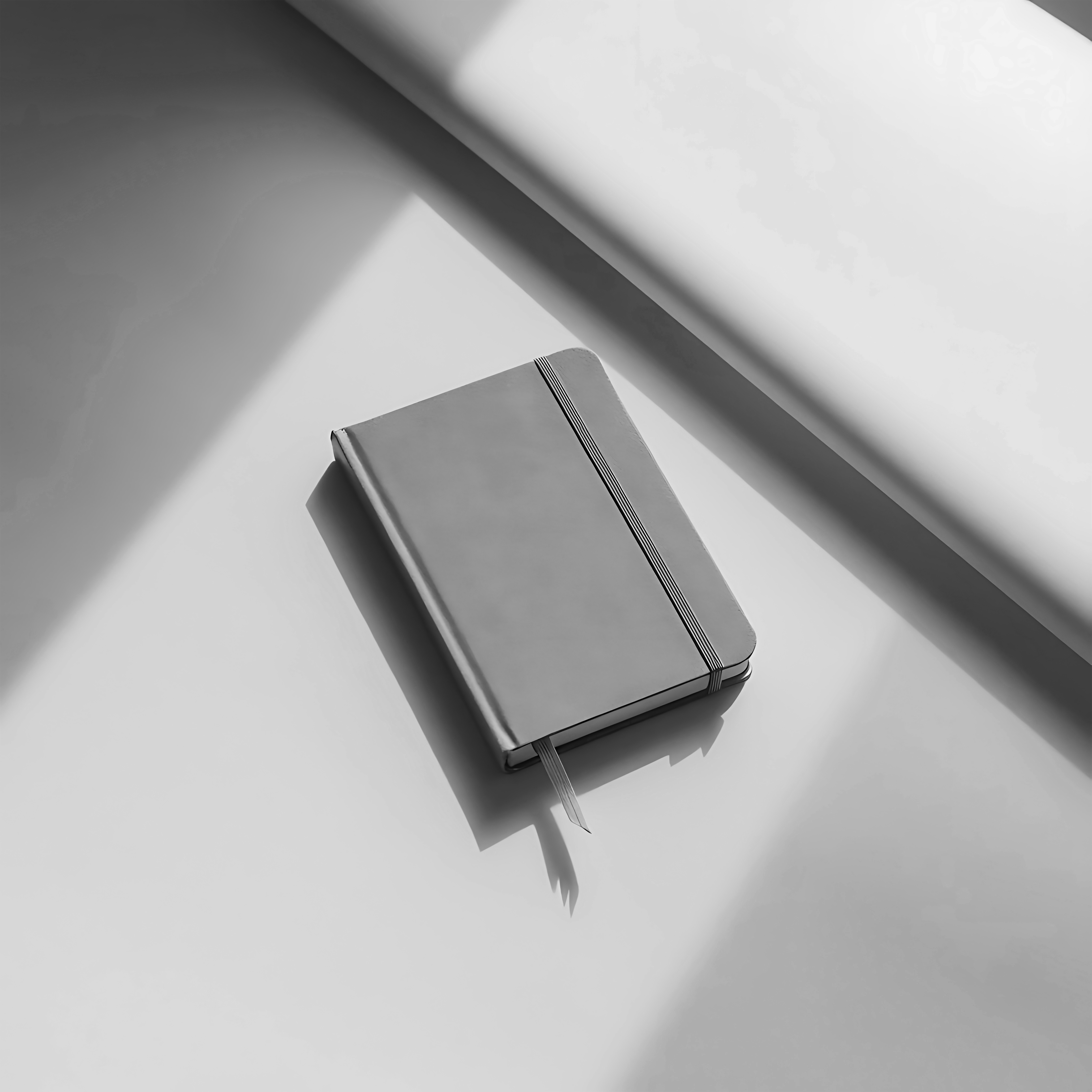 Kapalı ve lastikli bir not defteri, pencere kenarındaki beyaz yüzeyde ışık ve gölge oyunlarıyla duruyor.